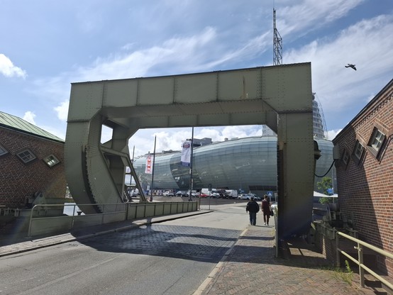 A futuristic, long and round building behind a gate on a bridge.