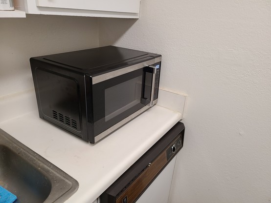Photo of a black microwave on a kitchen counter next to a sink. 