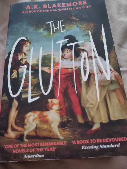 Copy of The Glutton by AK Blakemore. A 19th centuryish painting of a greenish, pauper child in rags approaching a boy and girl child who are dressed in finery. A dog looks on.