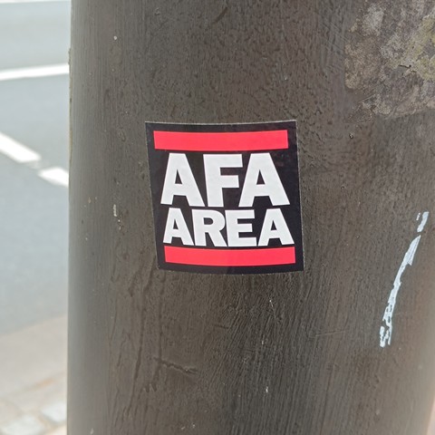 Sticker in a lamp post. Its square, black with white letters, and reads AFA AREA. AFA is the acronym for German 