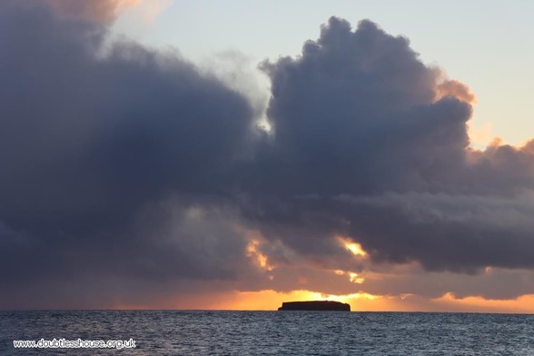 Photo of sunrise and cloud behind island on the sea
