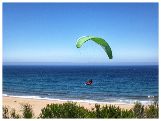 A paraglider floats beneath a green 'chute over a beach. Behind him (it was a 'he') is a blue sea under a clear sky. Taken with a Casio Exilim EX-Z65 6MP noughties digicam. 