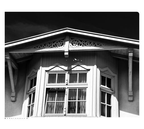 Schwarzweißfotografie: Giebelfenster an einem alten Haus, fein geschnitzte und verzierte Schmuckelemente in schneeweiß darüber, Bäderarchitektur an der deutschen Ostseeküste 