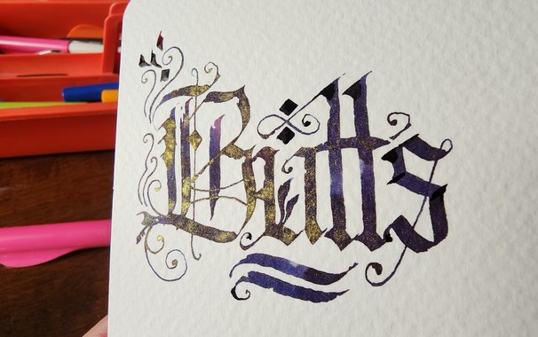 The word 'Butts' calligraphed in Blackletter script with an ornate capital B featuring swirls and leaves drawn with the pen nib. The ink is dark indigo with some lighter purple-pink bits, but has a strong gold shimmer when catching the light.