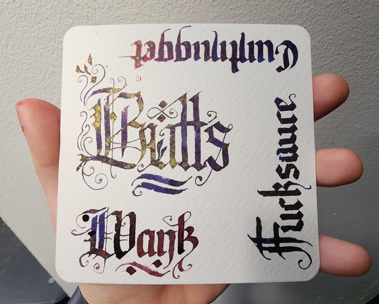 Showing the paper with the word 'Butts' the right way around and the other words framing around it. The light falling on the left side of the paper is catching the gold pigment in the inks.