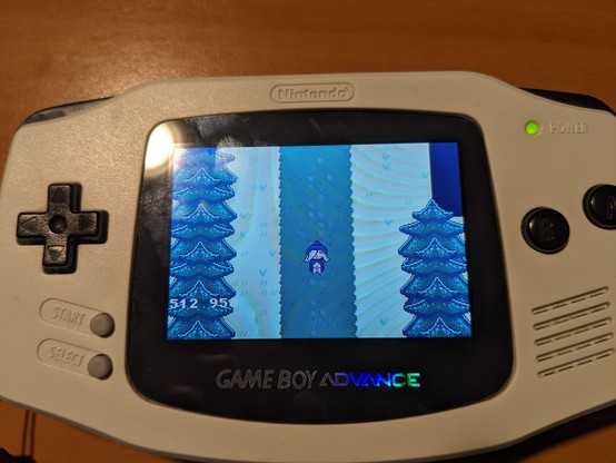 A picture of a white Gameboy Advance running a game with a witch in a snowy forest (and some debug numbers in the corner of the screen)