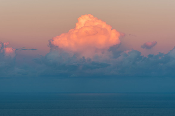 a giant cloud painted pink at the top over the ocean sinking in twilight blues.