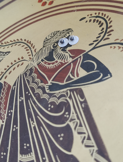 Foto eines Keramiktellers, bemalt mit Dionysos in antikem Stil (Rot-schwarze Glasir und Kratztechnik). Der Gott schaut mitvübergroßen Wackelaugen ganz drollig