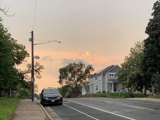 Photo of a sunrise in an urban residential street. No one is around and the sky is two weird shades of gray and orange