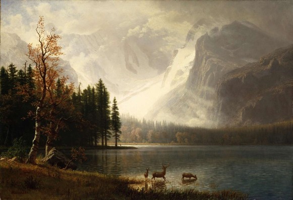 A serene lakeside scene is set against the backdrop of towering, snow-covered mountains. Three deer stand at the water's edge, with a lush forest stretching out beside them under a cloudy sky.