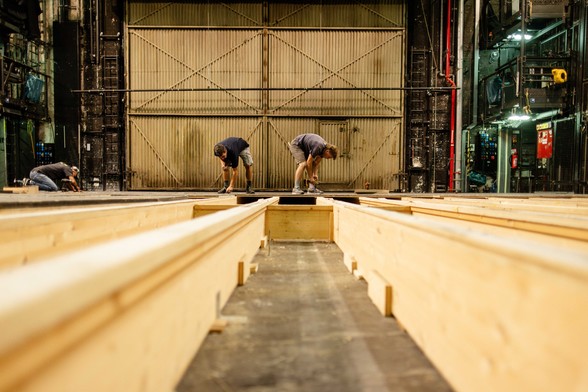 Zwei Personen arbeiten an den Bodenplatten der Bühne davor sieht man die offene Unterkonstruktion der Bühne aus Holz