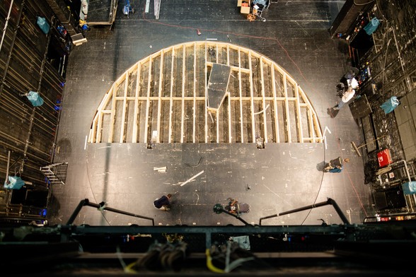 Perspektive von oben auf die Drehscheibe, die zur Hälfte offen ist und man siehr die Holzkonstruktion, Personen arbeiten an den Bodenplatten der Bühne 