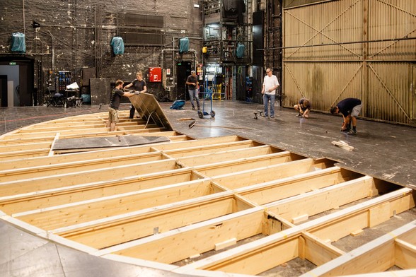 offene Unterkonstruktion der Bühne aus Holz, sechs Personen tragen die Bodenplatten der Bühne ab bzw. schrauben die Platten ab