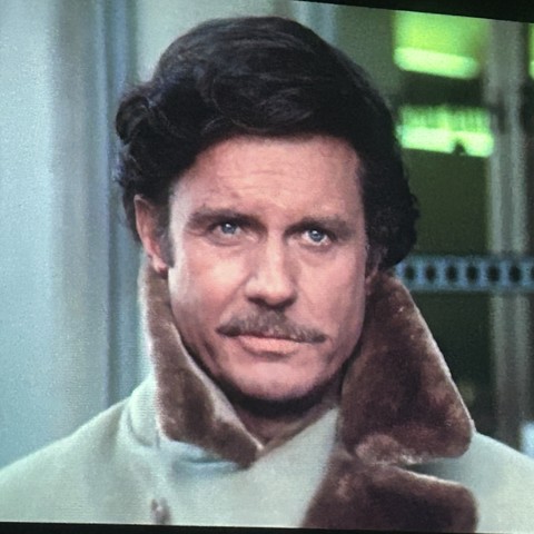 Actor Cliff Robertson in 3 Days of the Condor. A square head and shoulders capture from the movie projected on my wall. He is a white man with dark pompadour hair, a light brown mustache that matches the upturned fur collar on his khaki overcoat. 