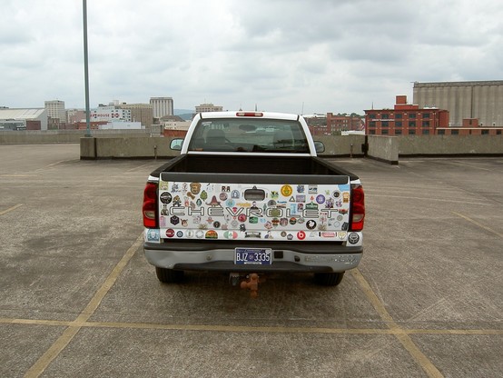 A pickup truck in an otherwise empty lot, at the top of the parking garage. The tailgate is plastered in stickers.