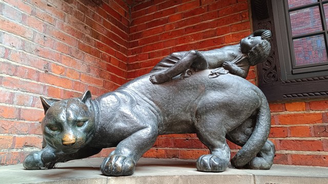 A bronze sculpture of a baby reclining on the back of a ready to pounce big cat.