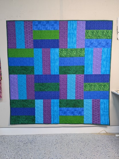 Lap sized quilt made from blue, purple, teal, and green fabrics. Each block is 3 strips, alternating vertical and horizontal layout. There are 16 blocks, arranged 4 across and 4 down.