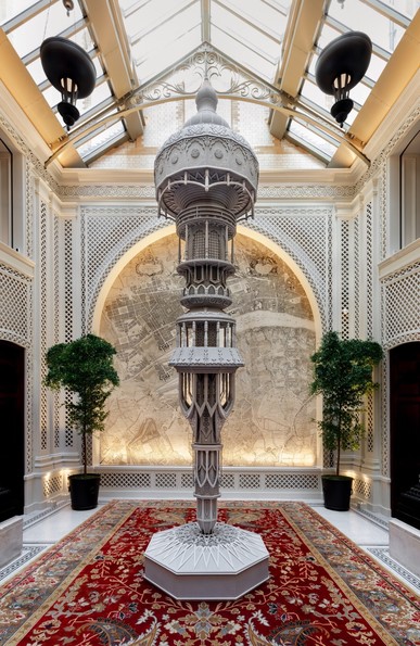 an ornate, architectural gray sculpture inspired by columns and design motifs from a wide variety of places, in the lobby of a luxury hotel