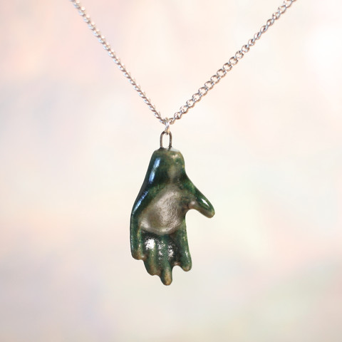A hand-sculpted ceramic hand pendant hanging from a silvery chain.