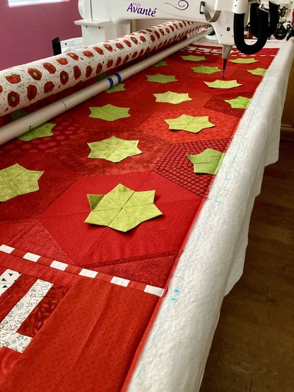 A red and green quilt on a longarm sewing machine, near, but not quite at the end. The visible quilt blocks are hexagons that resemble tomato pincushions