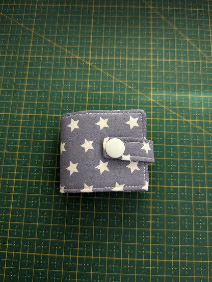 Outside of a small needle book, made from a grey cotton with little white stars. It's closed by a little loop from the same fabric with a white colour snap on the end.