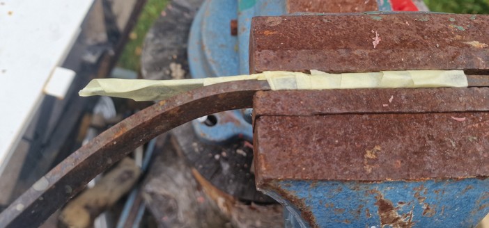 A knife blade taped together with a pre-bent iron bit in vice before cold bending. 