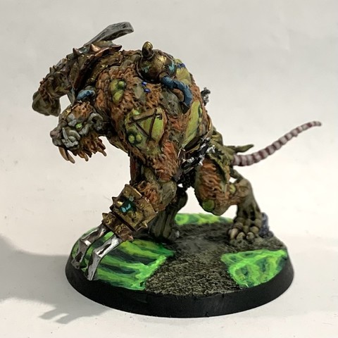 Large rat-man-monster in dark greens and browns. Its flesh is tearing away showing grotesque green-tinged skin and muscle. It has brass armor and weapons grafted to it. It walks over broken ground with green glowing waves in puddles. 