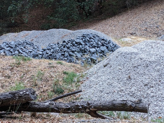 Gravel and larger rocks in piles, with a log across the foreground.