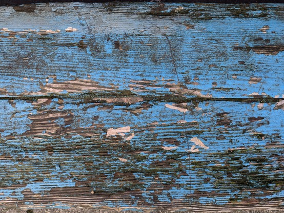 The seat of a bench, painted blue, but showing lots of wear and wood grain.