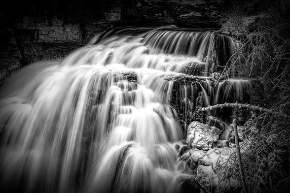 A close up black and white view of Inglis Falls near Owen Sound, Ontario as it crashes its way down the rocks and through the surrounding forest. 