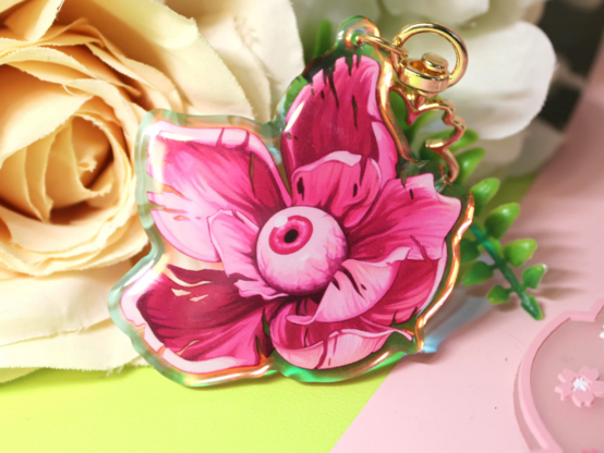 Acrylic charm: semi-realistically rendered pink flower with eyeball on green/pink background with deco flowers.