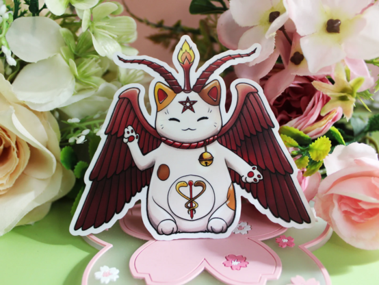 Sticker of a maneki-neko as baphomet on green/pink backdrop with flower decoration.