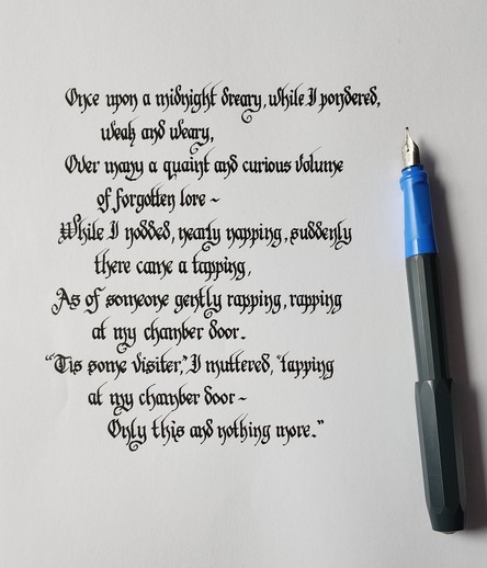 A snippet from Poe's 'Nevermore', calligraphed in a kind of textura-ish Blackletter script in black ink with the pen resting to the side;

Once upon a midnight dreary, while I pondered,
weak and weary,
Over many a quaint and curious volume
of forgotten lore -
While I nodded, nearly napping, suddenly
there came a tapping,
As of someone gently rapping, rapping
at my chamber door.
