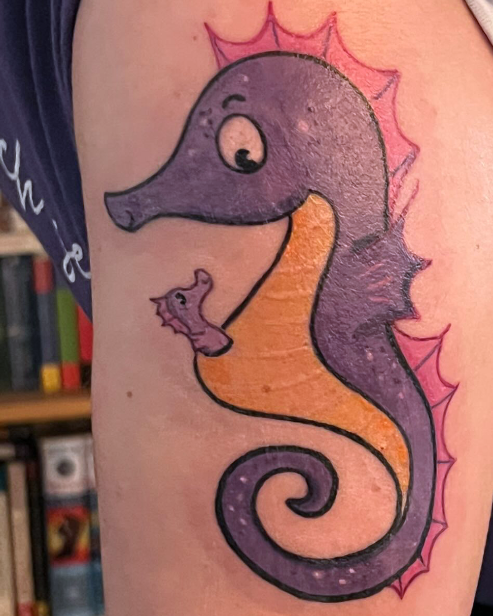 Foto eines frisch gestochenen Tattoos: Ein violettes Seepferdchen, aus seiner Bauchtasche schaut ein kleines Baby-Seepferdchen