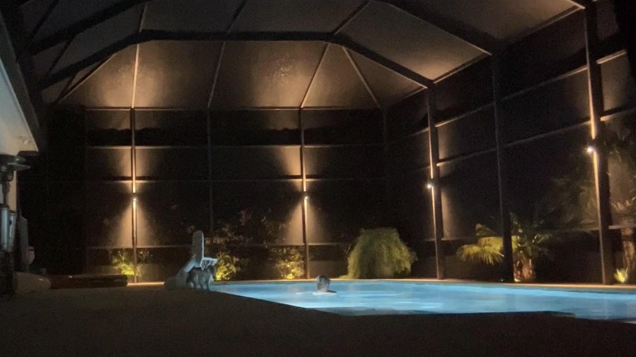 Large screen enclosure covering a bright blue lit swimming pool with a man me swimming in it