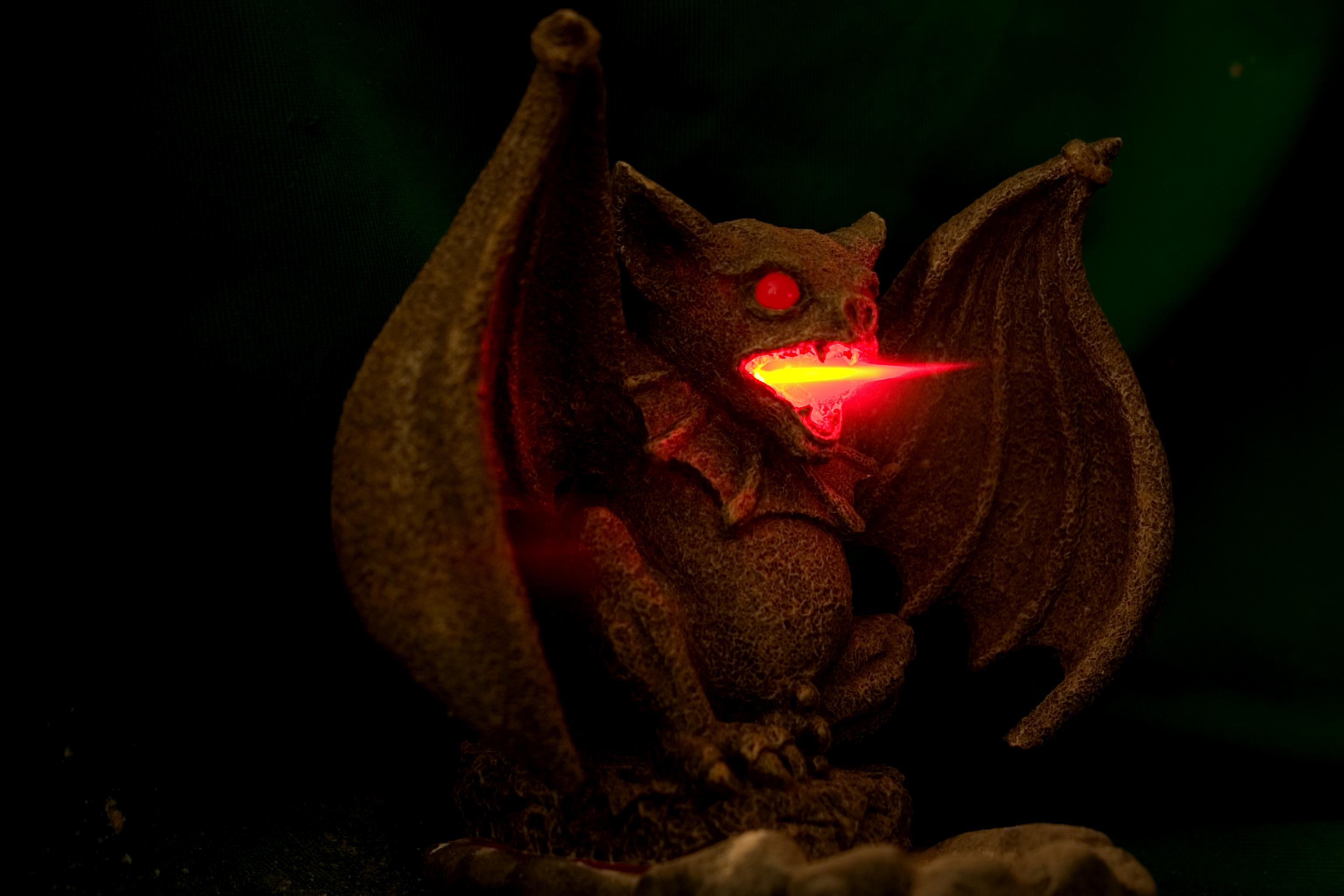 A photograph of a bat like gargoyle with a hint of smoke and red fire coming out of his mouth, his eyes glowing red as well. A photograph of a bat like gargoyle with a hint of smoke and red fire coming out of his mouth, his eyes glowing red as well.