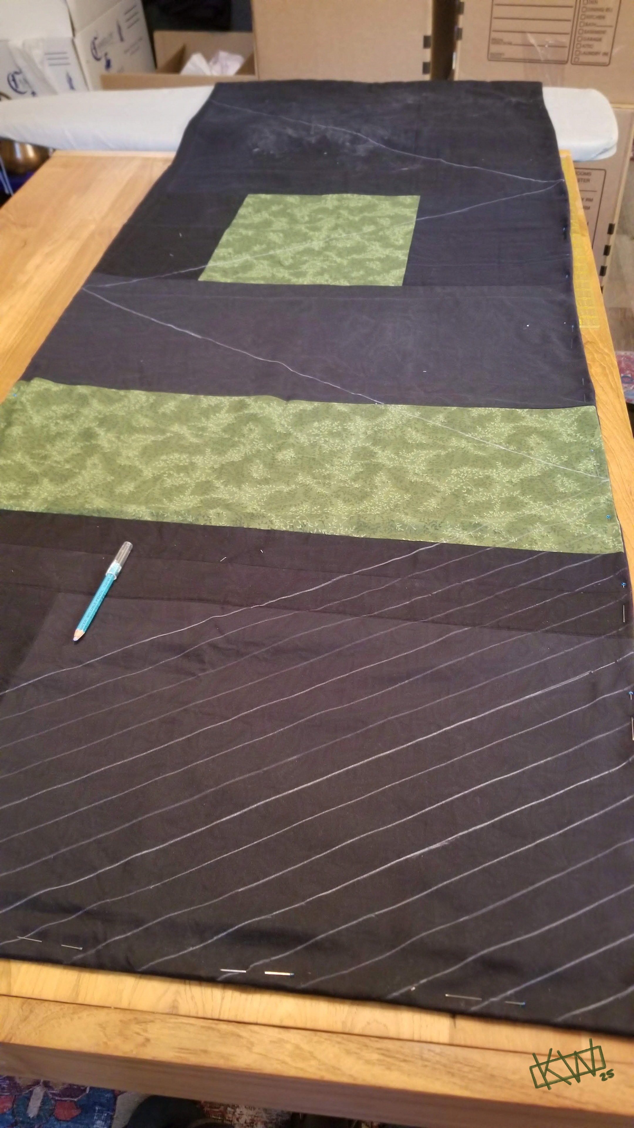 Photo of a long patchwork shawl, pinned around the edges, with a zigzag pattern partially drawn on in chalk.
