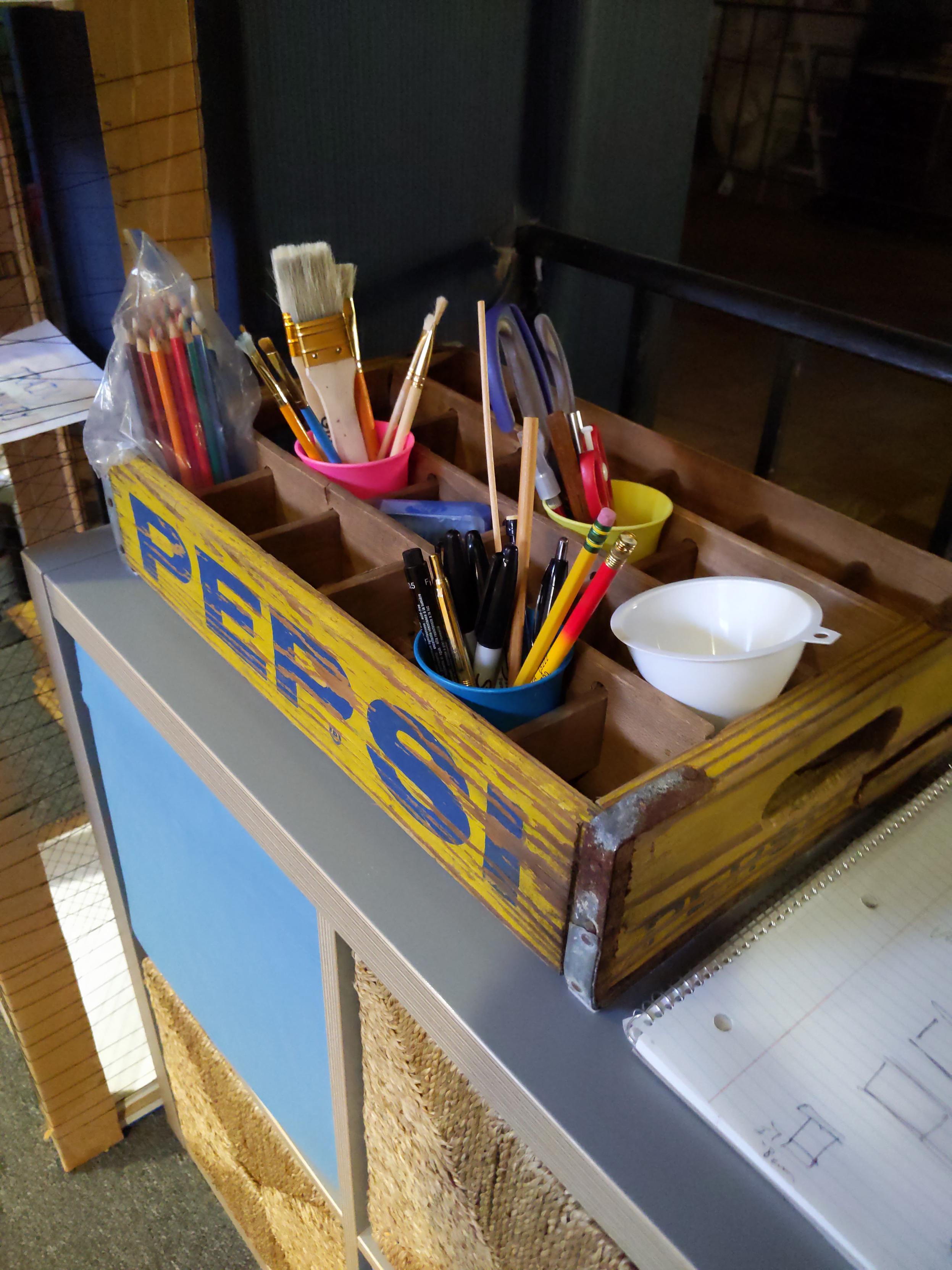 A crafting tool rack for the theater, made from a reclaimed cola crate. It's branded Pepsi on the side, in a style the company hasn't used in decades.
The corners are strapped with rusty metal.