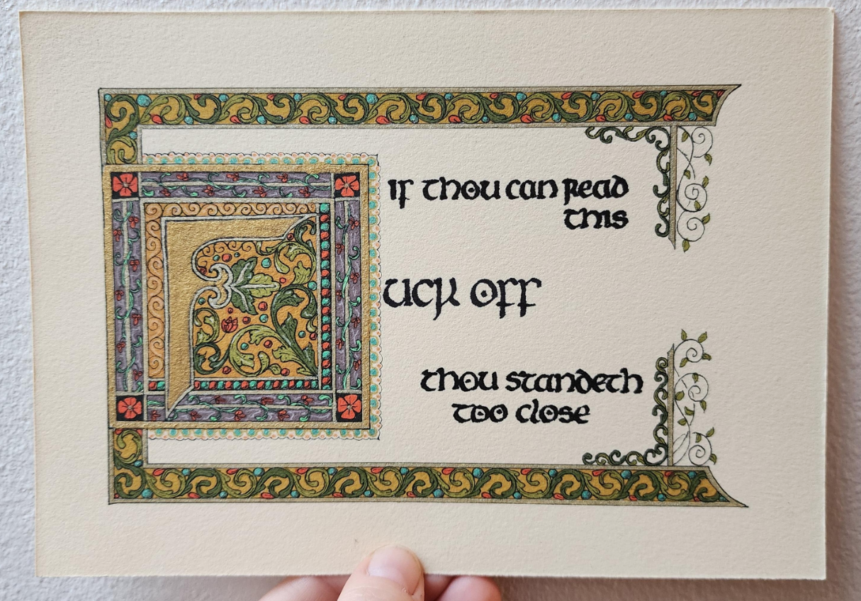 'If thou can read this, fuck off, thou standeth too close' calligraphed in black ink insular script. The 'fuck off' part is bigger and with a big ornamental F in gold in its own decorated box. There's a border of swirling leaves across the top and bottom, and bars with vines hanging down and up on the right, framing the text.