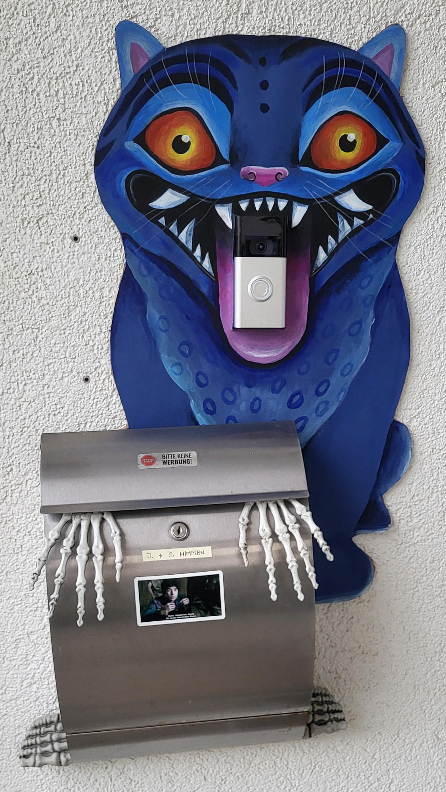 Selbstgebastelte Halloween-Deko am Briefkasten. Auf Pappe gemalter Derpy, der Dämonen-Tiger aus dem Film Kpop Demon Hunters. Es sieht aus, als würde die Klingel auf seiner Zunge liegen.