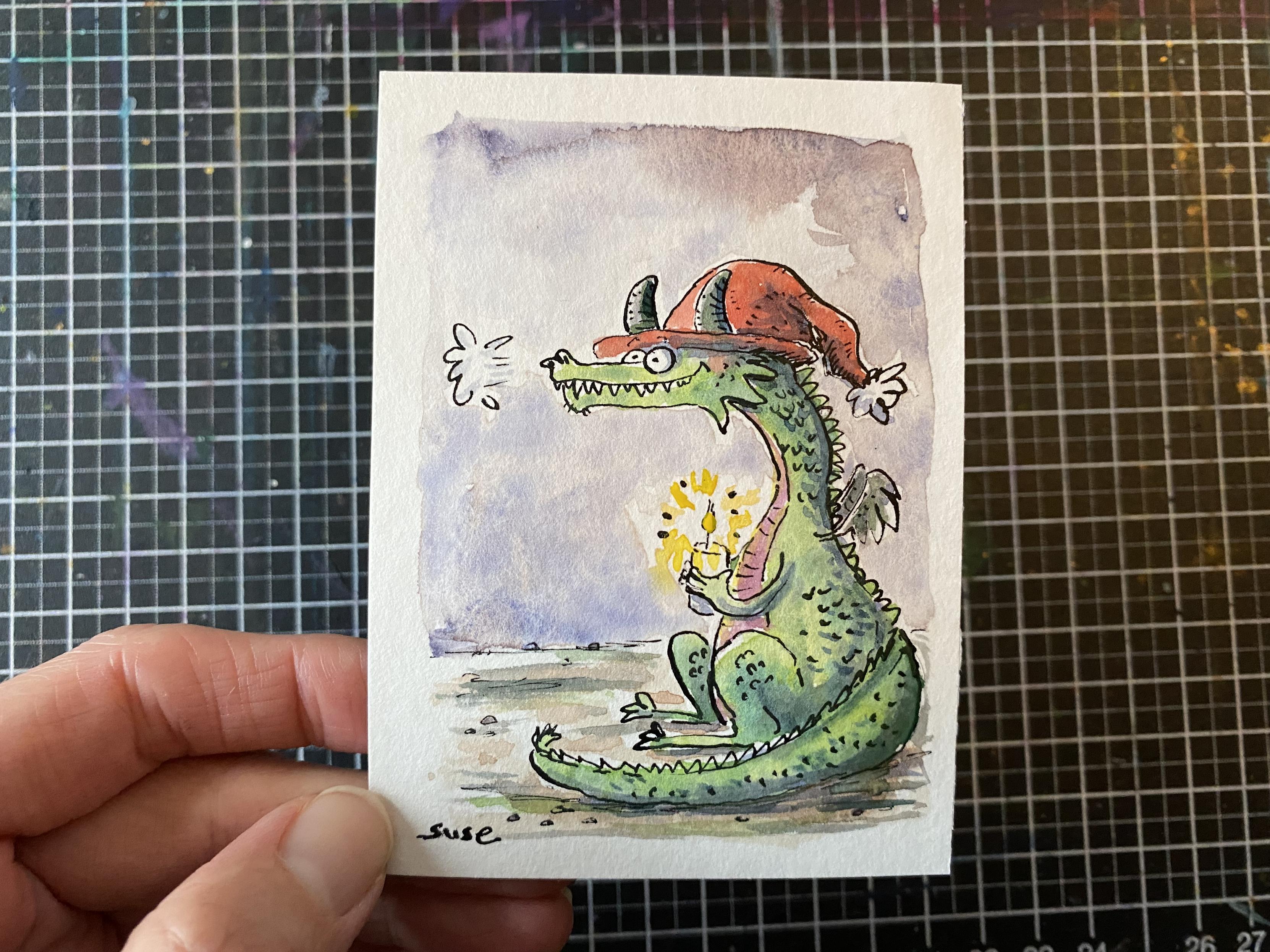 Ein grüner Drache mit roter Mütze, der eine Kerze fest hält.