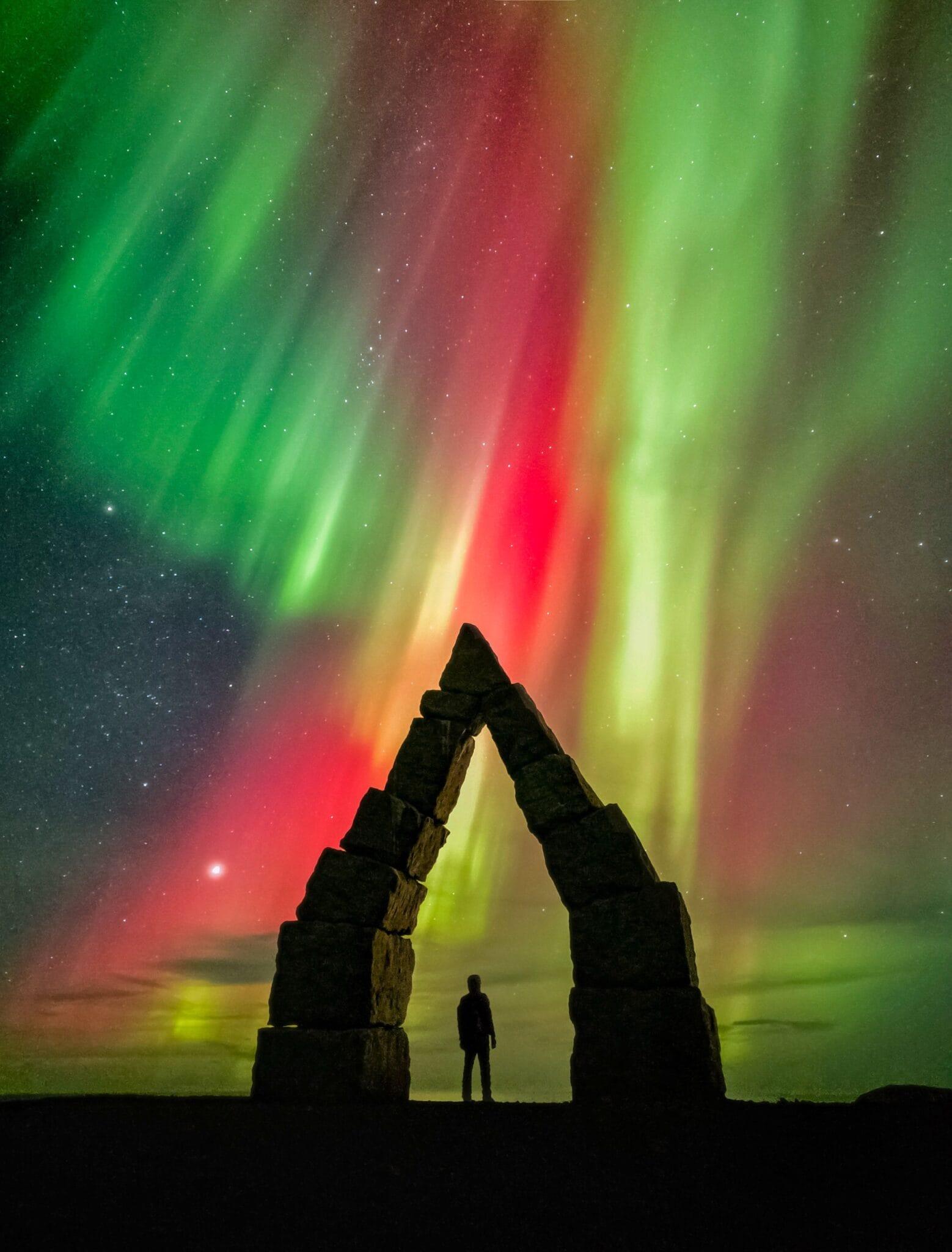 Green aurora borealis over a snowy, forested landscape