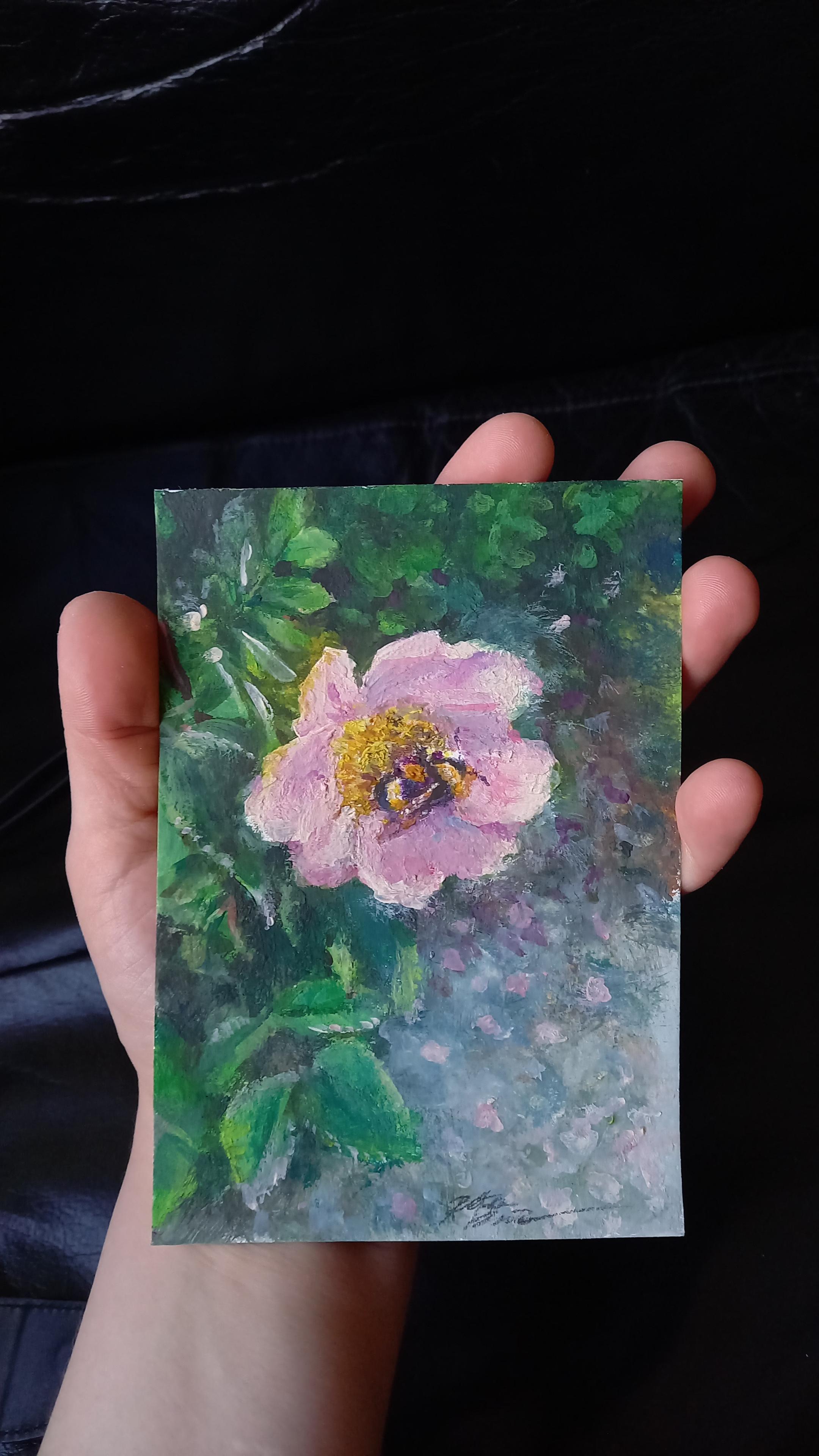 Hand holding a card sized gouache painting of a bumblebee on a rosehip flower.