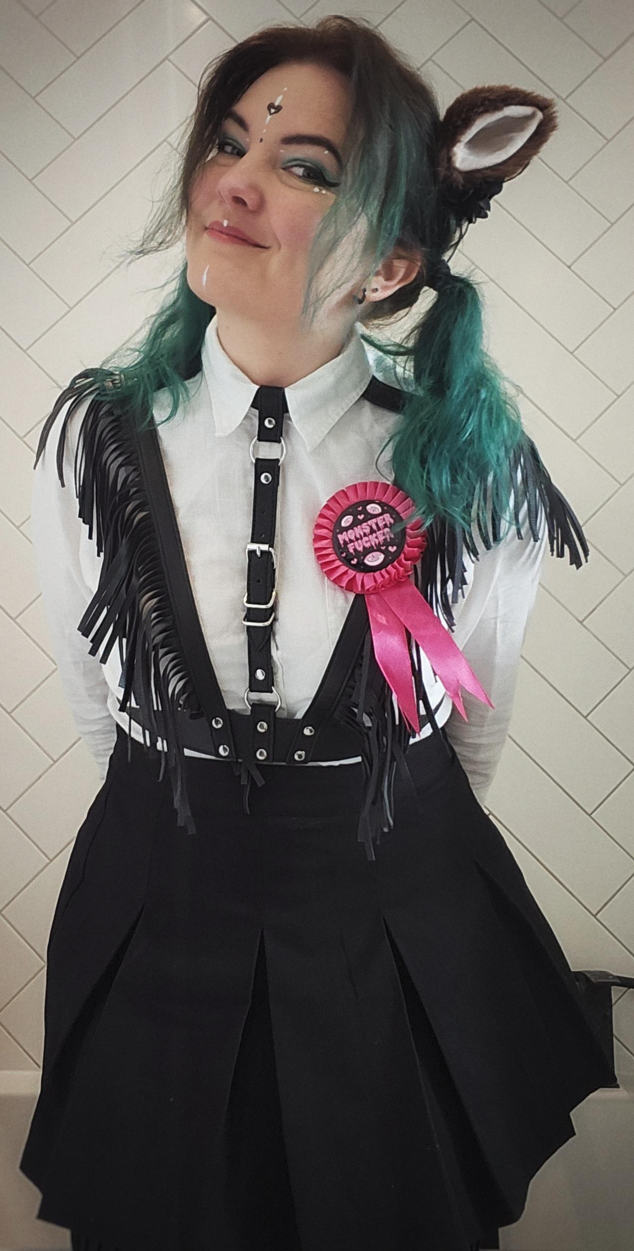 Jen in catgirl ears, a white shirt buttoned all the way up, and a harness over that, giving her hints of British Police Officer, except she's got like cowboy frills and a pink medal that says MONSTER FUCKER