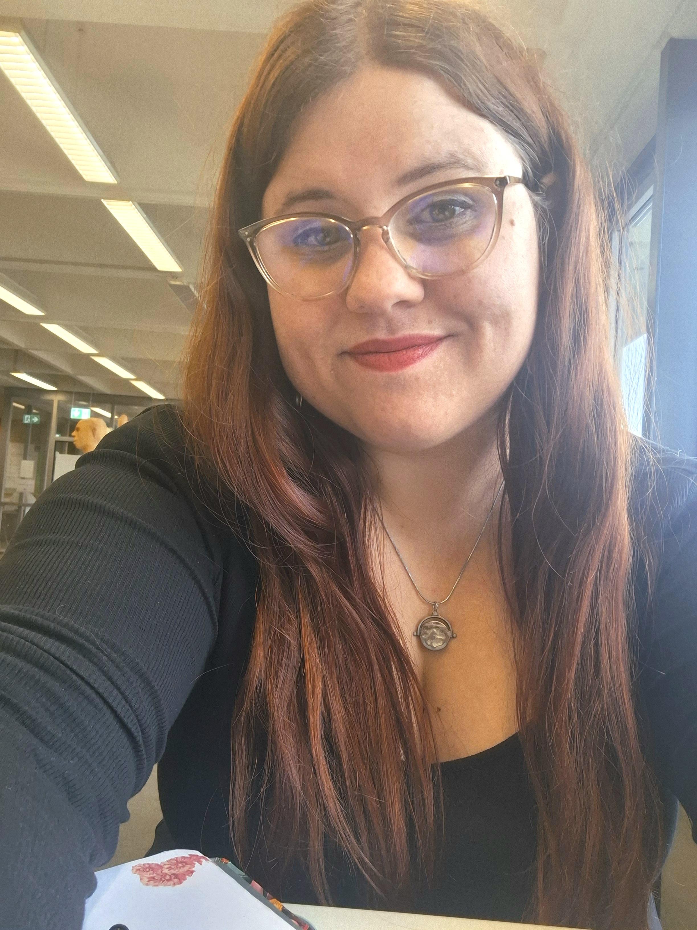 Selfie of a red-haired woman with glasses in a library.
