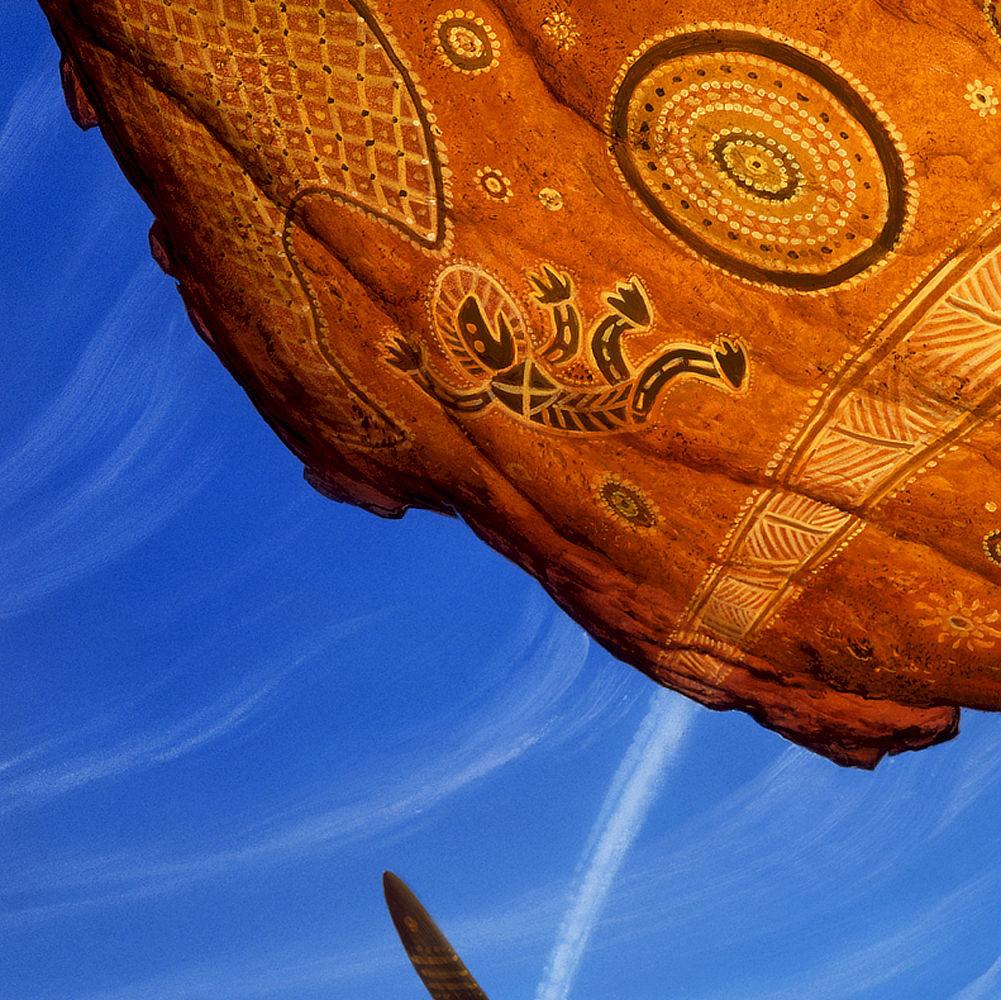 Background detail from SKYCHILD’S FALL featuring pictographs on the orange rock above the main figure that consist of decorative shapes and narrative elements. The most prominent image features a figure falls with arms and legs flailing.