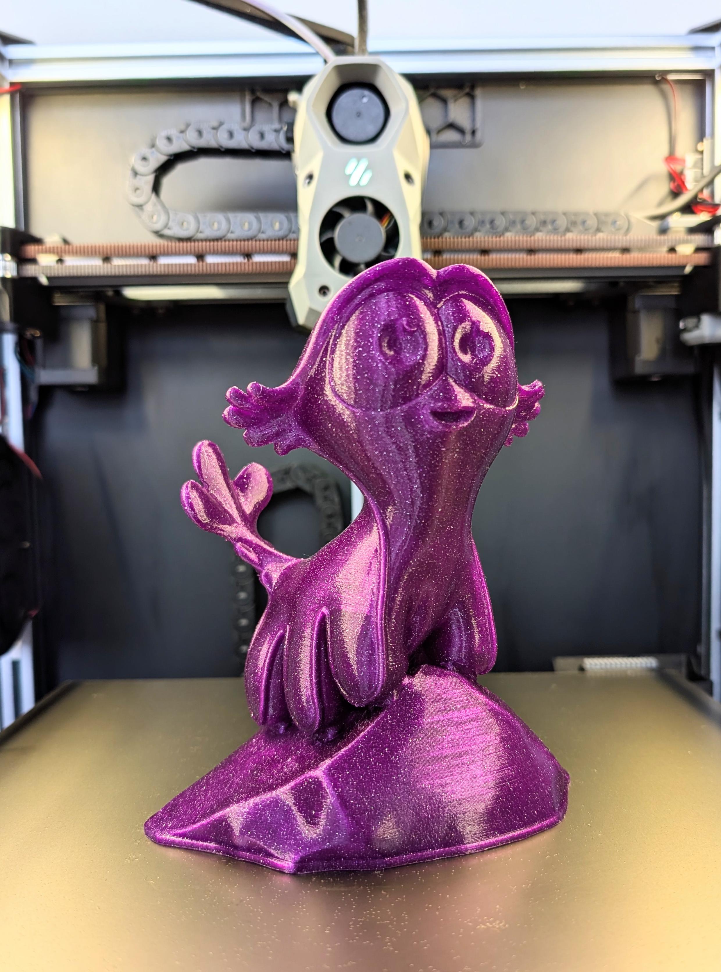 A 3d printed figurine standing on the print bed of a 3d printer. It is purple and sparkly, illuminated by LED lights