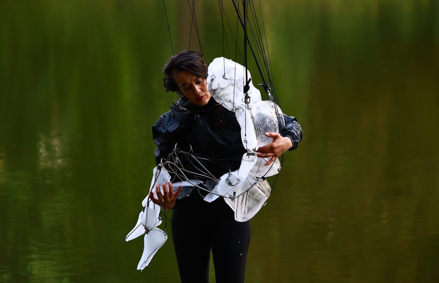 a photograph of a dance performance with a woman in black clothing, cradling a puppet made from ice