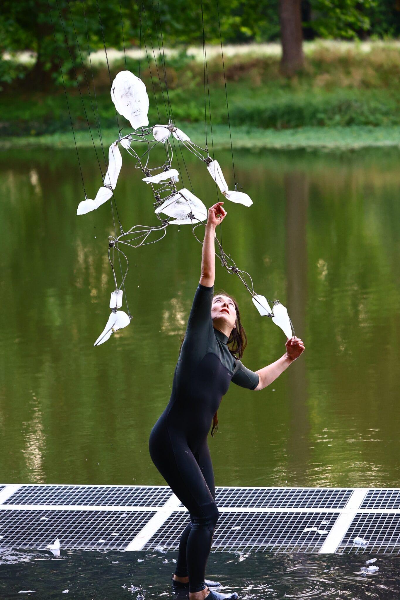 a photograph of a dance performance with a woman in black clothing, cradling a puppet made from ice