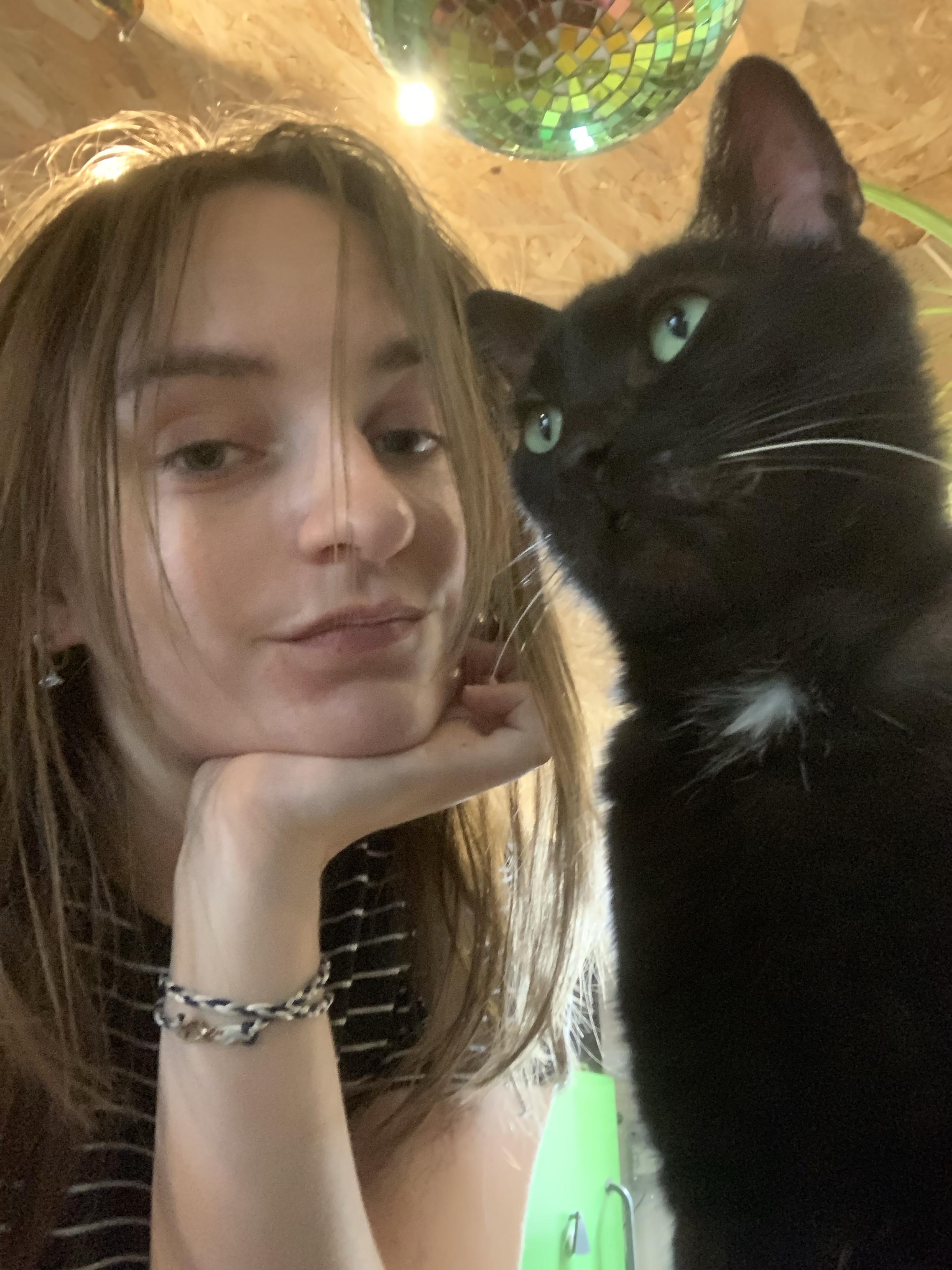 Photo de moi (Minna) avec un chat noir au yeux vert (Charbon) et une boule disco en haut 
On est dans l’atelier
